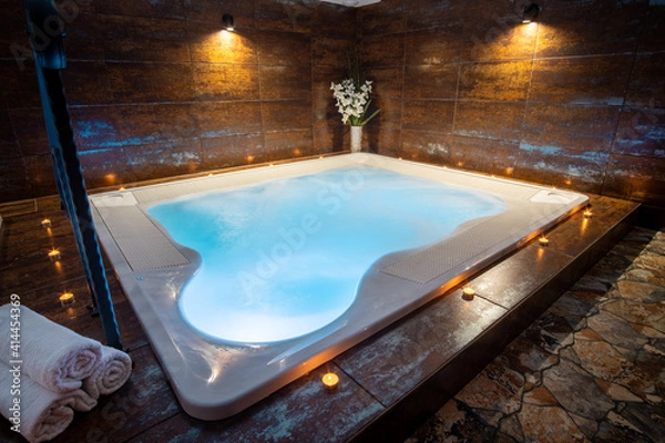 Fototapeta Private whirlpool in a wellness center. Indoor jacuzzi with bubbles. Candles around a whirlpool with blue water. 