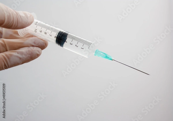Fototapeta Medical syringe loaded and ready to inject held by a gloved hand on a white background.