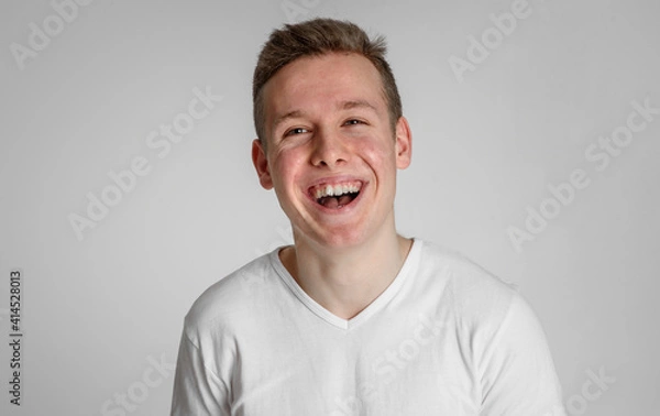 Fototapeta 
teen guy looking into the frame happy surprised can't believe raised eyebrows
 and sincerely smiling with teeth on a white background in a white T-shirt