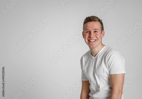 Fototapeta 
teen guy looking at camera happy
 and sincerely smiling with teeth in the right side of the frame on a white background in a white T-shirt