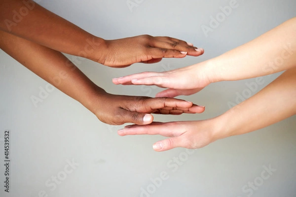 Fototapeta outstretched two diverse female hands holding on top of each other, women keeping empty palm on gray isolated background. people diversity, help, support, love concept
