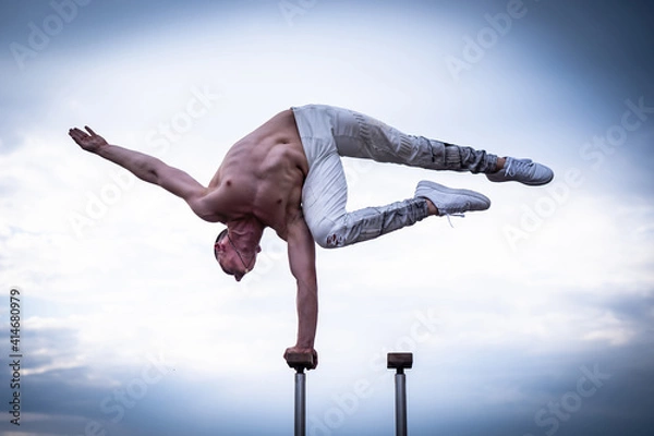 Fototapeta Circus artist keeps balance on one hand on the cloudy sky background. Concept of handstand, performing and art