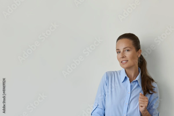 Fototapeta Smiling a female with strong hair, looking at the camera. Studio shot of a beautiful woman, isolated from the empty studio wall. She standing on the right side.