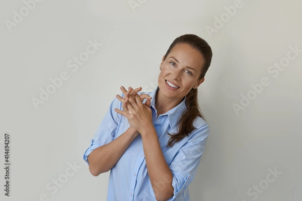 Fototapeta Happy young woman posed against a gray wall. She smiling and looking on the camera with crossed arms with copy space