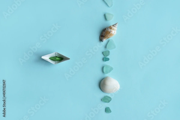 Fototapeta Paper ship, sea shell and stones isolated on blue background. Sea and vacation concept.