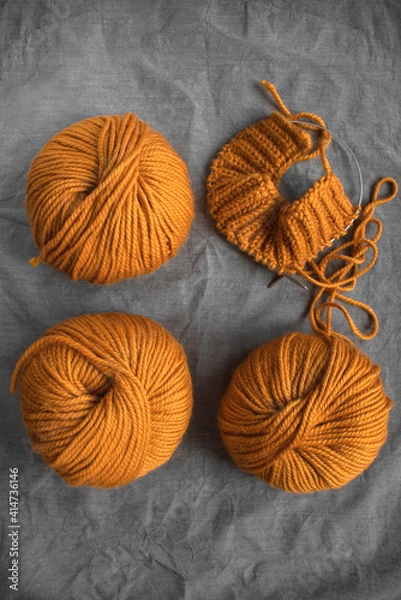 Fototapeta bright balls of orange woolen thick yarn and knitting on a gray wrinkled background with place for text