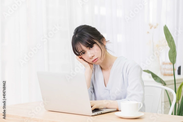 Fototapeta 部屋でノートパソコンを使いながら悩む女性