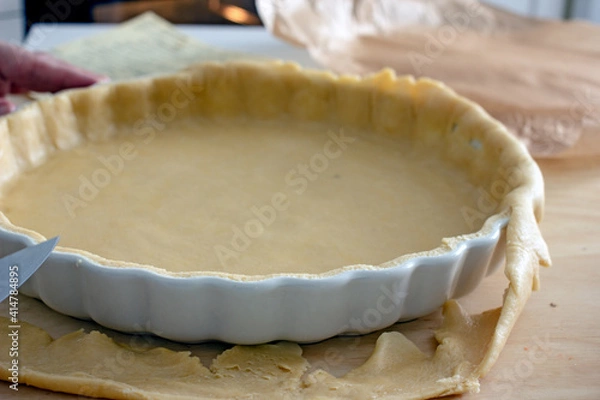 Fototapeta The process of making a base for a shortcrust quiche pie, male hands transfer a rolled dough sheet into a baking dish. Authentic home hobby home baker. Pie crust recipe
