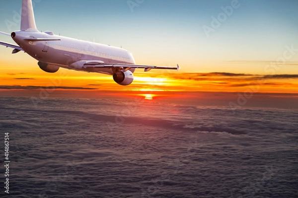 Fototapeta Commercial airplane jetliner flying above dramatic clouds in beautiful light. Travel concept.