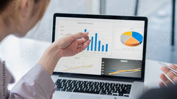 Fototapeta Business women point to the graph on their laptop at a meeting to discuss the market situation.