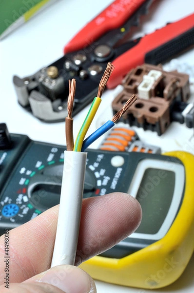 Fototapeta stripped, electrical three-core wire in hand against the background of terminal blocks and tools. close-up.