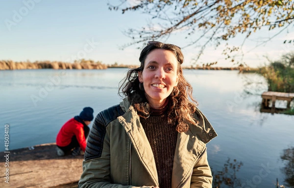 Fototapeta A mother and her son in a red hat and shirt are playing with the lake water on the pier