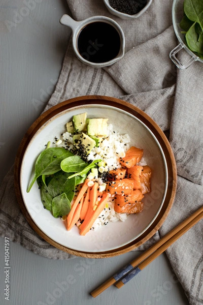 Obraz Poke bowl full of Chopped salmon and avocado mixed with rice, spinach leaves and carrot sticks.