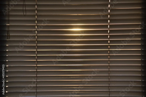 Fototapeta Sunlight through the closed blinds by the window