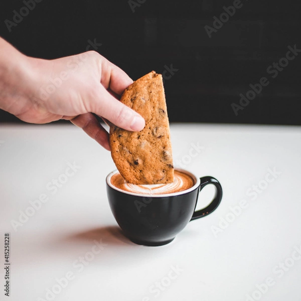 Obraz person holding a cookie oin coffee
