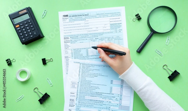 Fototapeta The person writes on the 1040 tax form. There are a lot of stationery and a calculator on the table. 1040 Individual Income Tax Return 