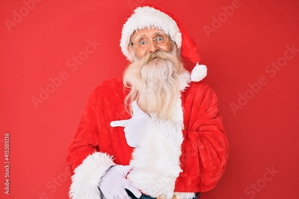 Fototapeta Old senior man with grey hair and long beard wearing traditional santa claus costume cheerful with a smile of face pointing with hand and finger up to the side with happy and natural expression