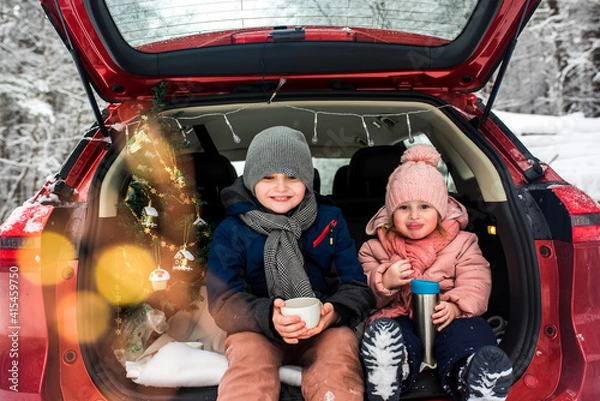 Fototapeta children in the trunk of a car in winter, christmas tree and snowman, merry holidays, hot tea and gingerbread, picnic in the forest