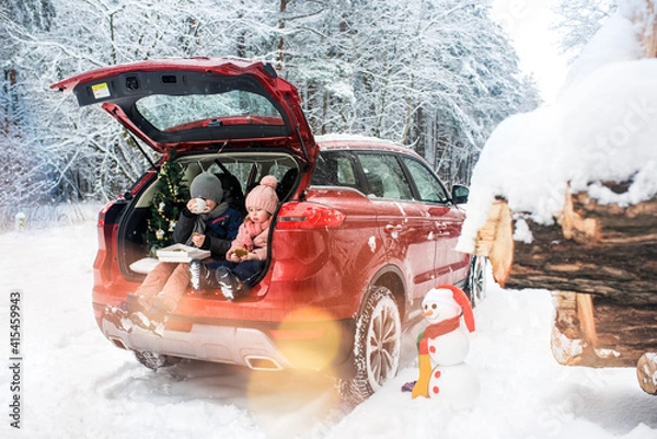 Fototapeta children in the trunk of a car in winter, christmas tree and snowman, merry holidays, hot tea and gingerbread, picnic in the forest