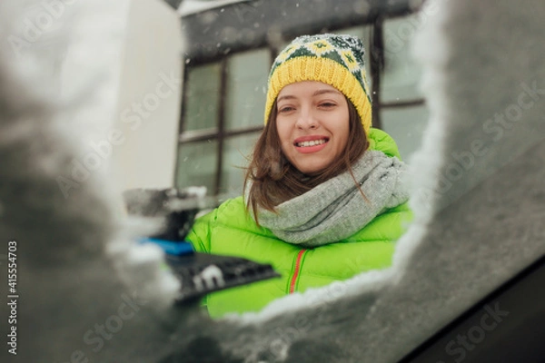 Fototapeta Girl with emotional face cleaning the windshield of a car from snow.