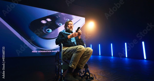 Fototapeta Mature speaker with disability showing new cellphone on stage