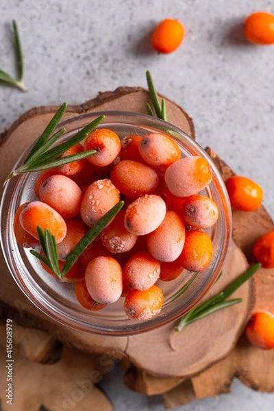 Fototapeta Illuminated frozen sea buckthorn with rosemary leaves on a wooden stand
