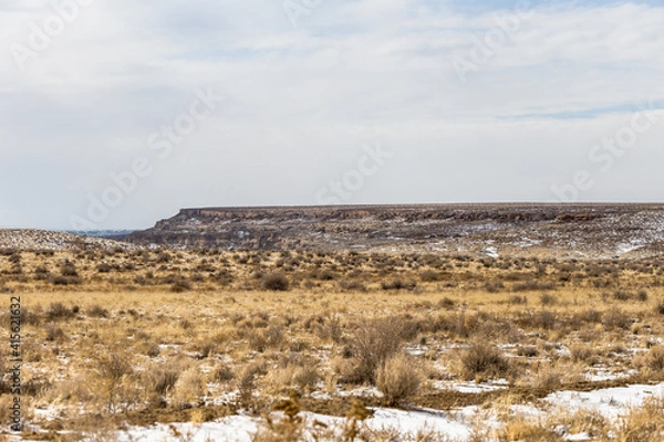 Fototapeta Yellow grass and brush with patches of snow on wide open desert vista landscape in rural New Mexico on cloudy day