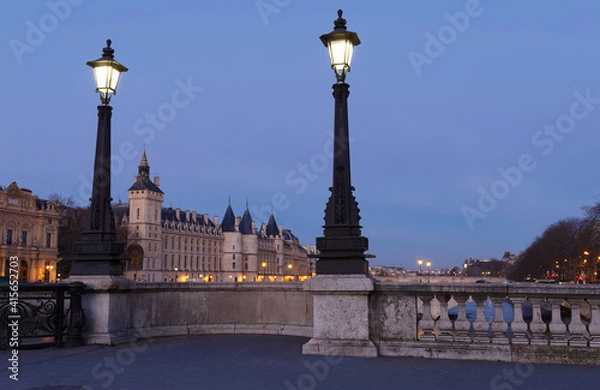 Fototapeta View of Paris by night with a bridge over the Seine river and the Conciergerie building.