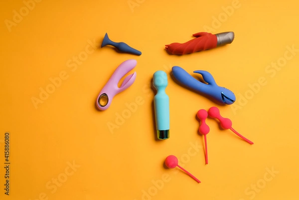 Fototapeta An abundance of multi-colored dildos and kegel balls on a yellow background. Clitoris massager, sex toys to maintain women's health. Space for text