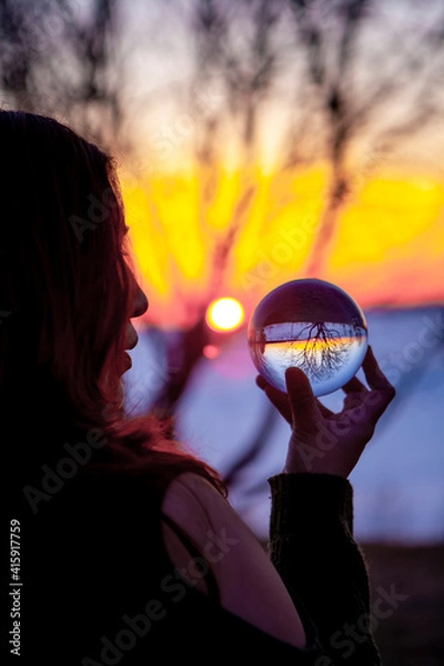 Obraz Native Girl looking into Crystal Ball on the Shore of a frozen Lake with a Magical Sunset
