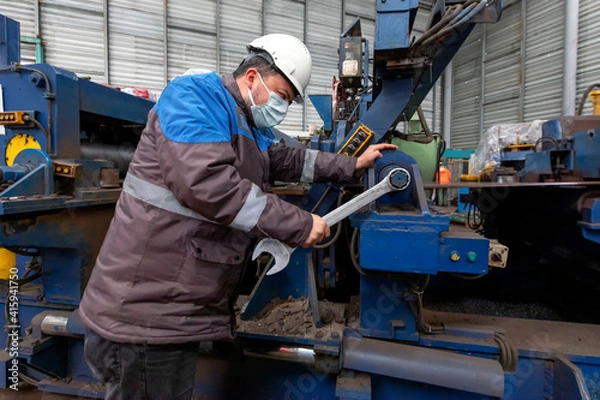 Fototapeta Worker is repairing to machine with screw wrench. A wrench or spanner is a tool used to provide grip and mechanical advantage in applying torque to turn objects usually rotary fasteners, such as nuts.