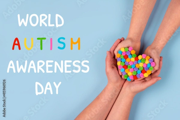 Fototapeta World Autism Awareness Day concept - autistic child's hands supported by mother holding multicolored heart on blue background. Autism spectrum disorder and child mental health concept, selective focus