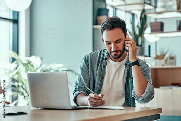 Fototapeta Focused businessman making notes in notebook at cafe