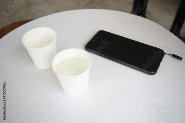 Fototapeta two white paper cups in cafe coffee table with mobile phone