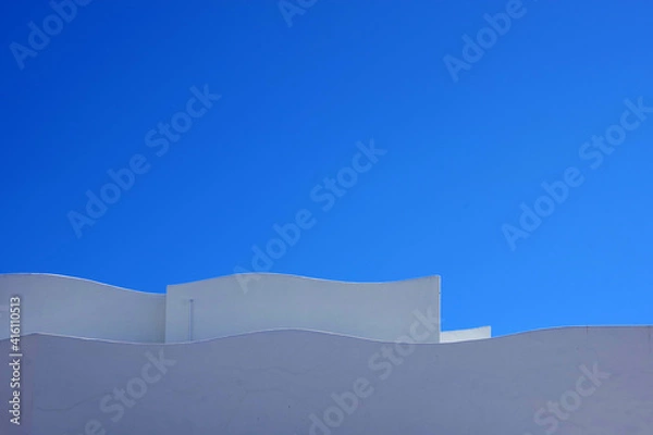 Fototapeta Partial view of the wave shaped top of a large white building complex and blue sky above