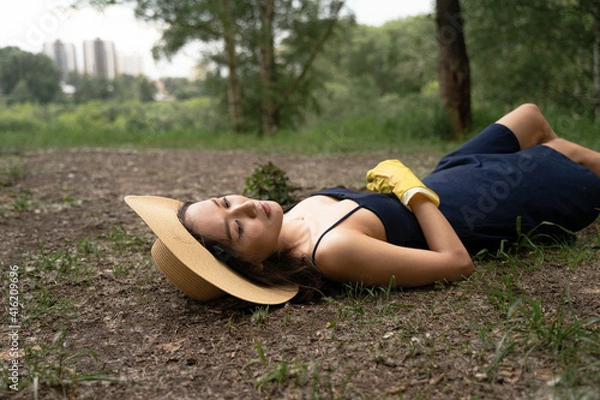 Obraz a girl of Asian appearance in a straw hat and yellow gloves lies on the ground in a dress