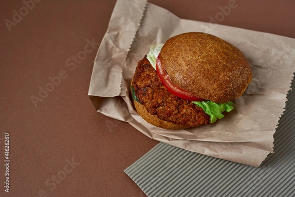 Fototapeta Vegetarian burger made rolled oats, chick peas, crushed onions and garlic, tomatoes, spices on a whole wheat bun and salat on the paper bag. Copy space. Healthy food concept.