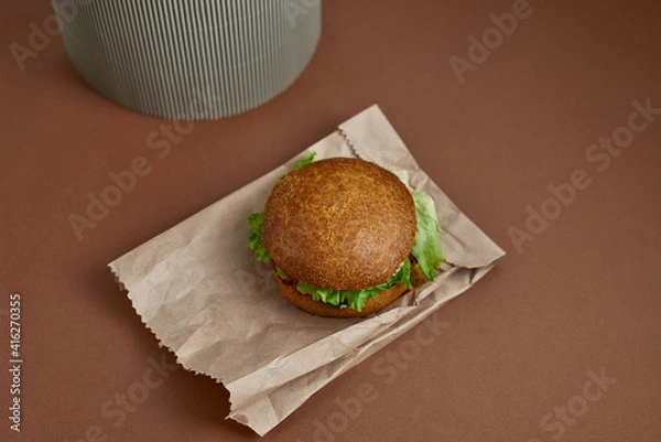 Fototapeta Vegetarian burger made rolled oats, chick peas, crushed onions and garlic, tomatoes, spices on a whole wheat bun and salat on the paper bag. Right side. Top view. Concept background