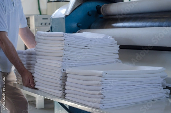 Fototapeta Unrecognizable man stacking freshly ironed sheets or fabrics in an industrial laundry.