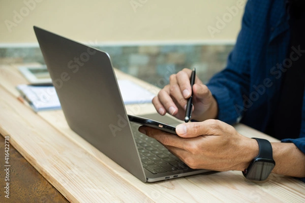 Fototapeta Hand using phone with laptop working at home