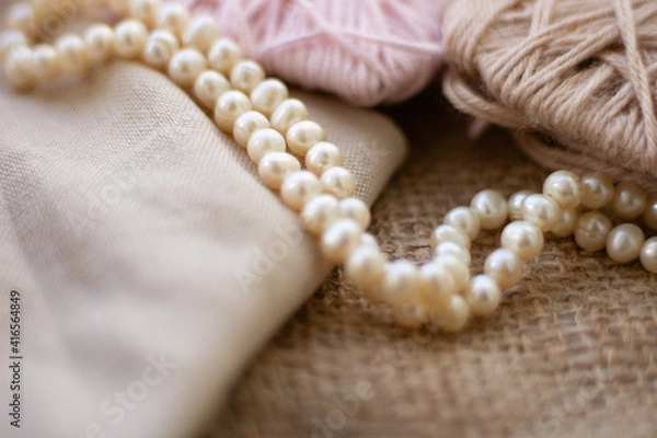 Fototapeta Cuts of yarn and thread on the background of burlap. Beige and soft pink colors of woolen and acrylic threads. There are pearl beads on the balls. Still life. Sackcloth. Fabric background