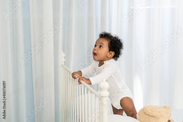 Fototapeta Happy African American Little baby boy climb the head of the bed and looking for some thing to learn