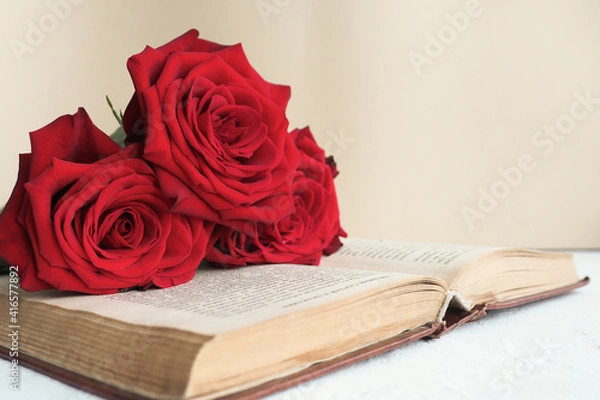 Obraz three red roses on an open old book on a table on a beige background..copy space.