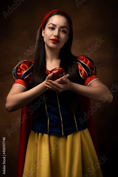 Obraz A girl in a princess costume holds a red apple. A brunette. Fairy tale. Red lipstick.