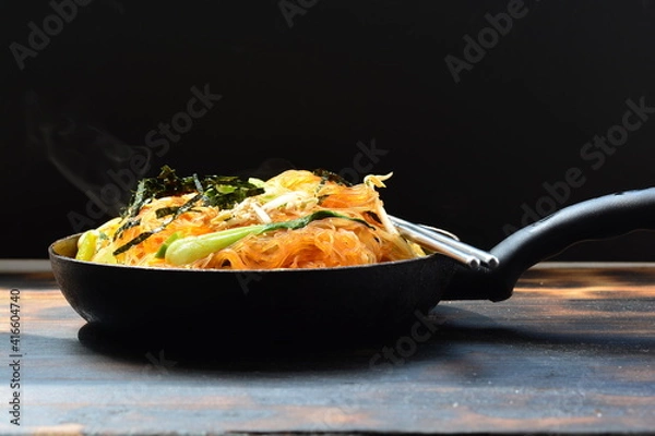 Fototapeta fried noodles with vegetable in a pan with black background and a chopstick.