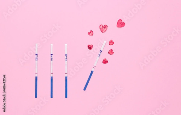 Fototapeta Negative and positive pregnancy test strip and red hearts on a pink background, top view. Waiting for the birth of a child