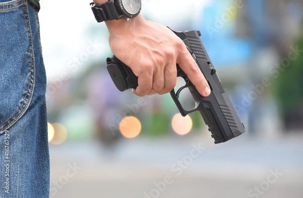 Fototapeta Automatic 9mm pistol holding in hand with blurred street bokeh background. Concept for robbery on the road and security profession.
