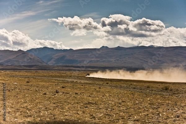 Obraz Autotourism, off-road in the mountains. The car drives through the valley between the mountains, leaving a dusty trail