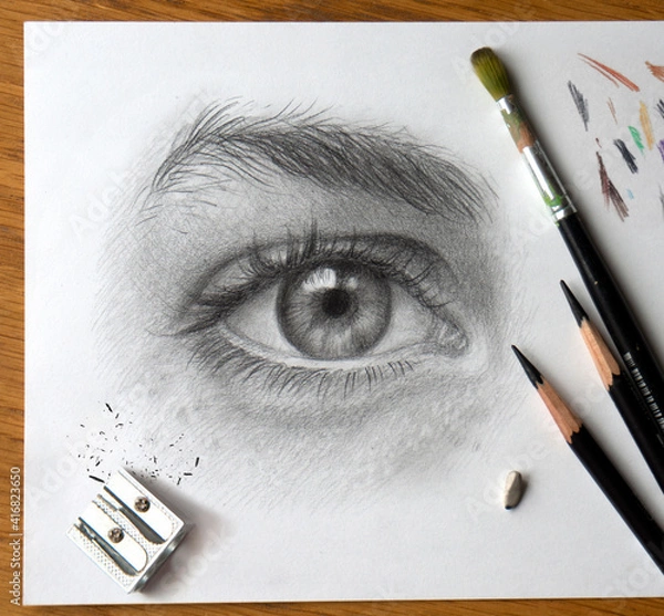 Fototapeta Realistic drawing of a human eye. Monochrome hand drawing. The process of working on the artist’s desktop with art materials.