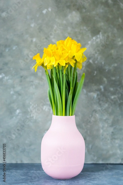 Fototapeta Yellow daffodils spring flowers in a vase on a grey background. place for text. vertical photo. Easter concept. Copy space. 
